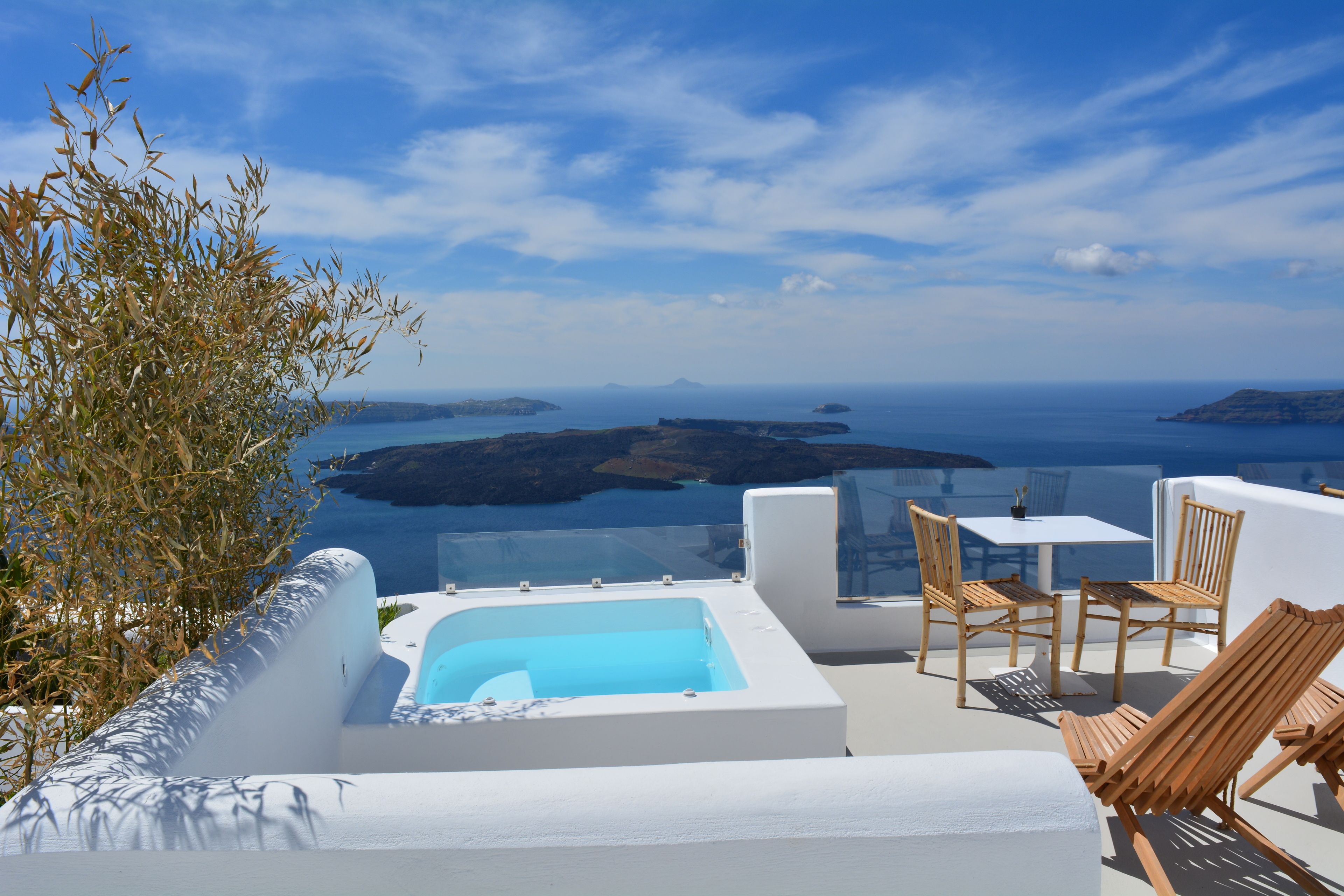 Une terrasse sur le toit dotée d’un jacuzzi, de chaises en bois et d’une table offrant une vue panoramique sur les îles et la mer.