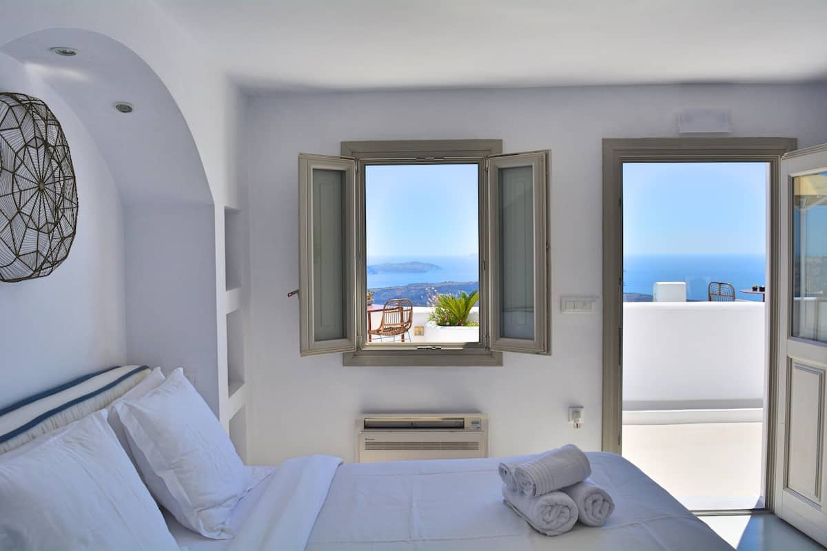 Una habitación de hotel con cama, ventana con persiana abierta, equipo de aire acondicionado y vista al mar.