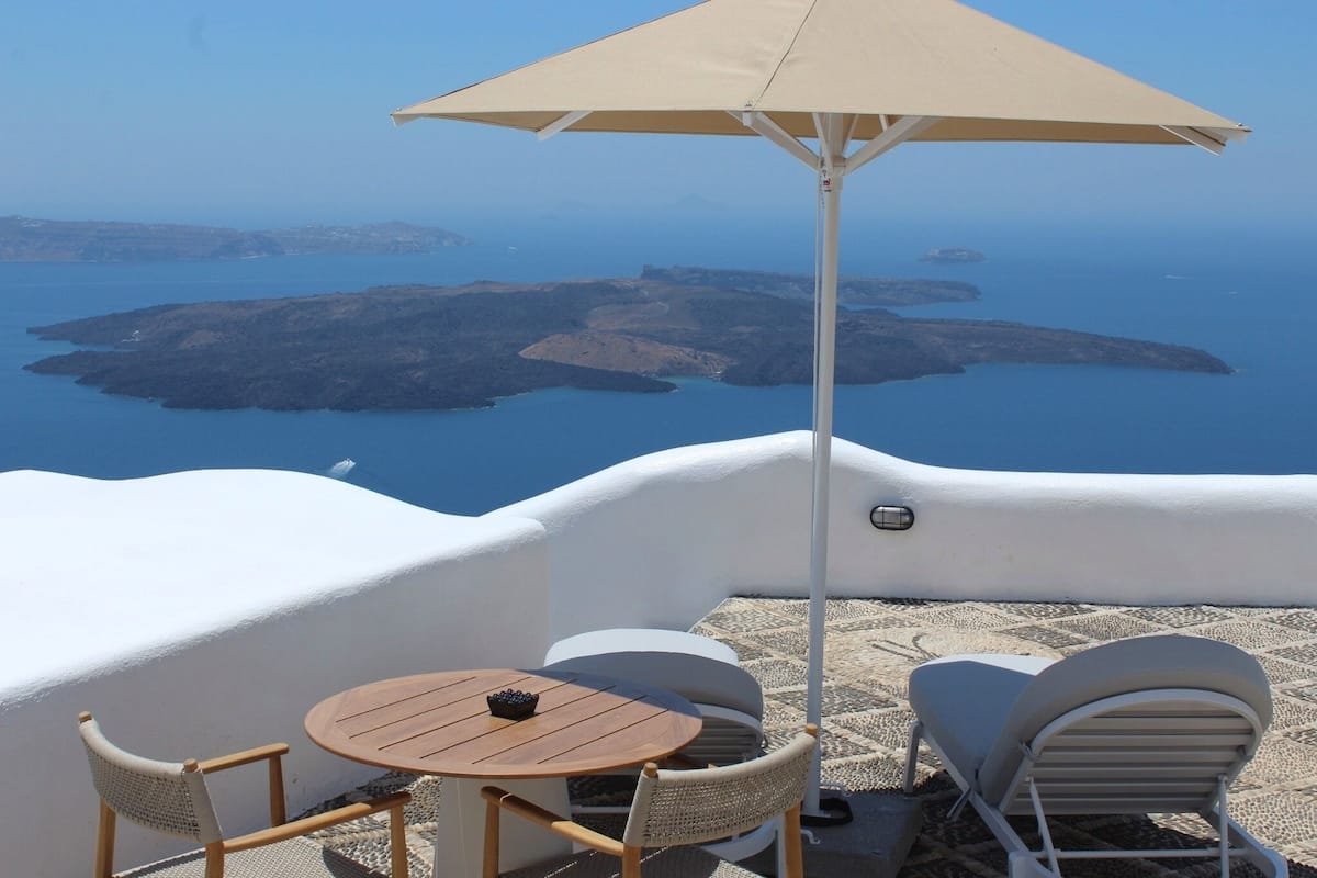 Una terraza con mesa, sillas y sombrilla con vistas al paisaje costero.