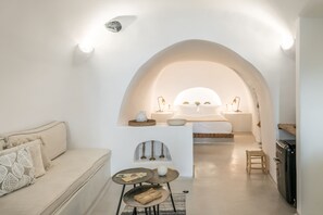 Ein modernes, minimalistisches Wohnzimmer mit Sofa, einem kleinen runden Tisch und einer Küchenzeile inklusive Kühlschrank.