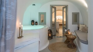 Un baño moderno y bien iluminado con una bañera independiente, velas y una mesita de mimbre.