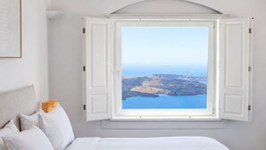 Un dormitorio con una cama grande, ropa de cama blanca y vistas a un paisaje costero a través de una ventana abierta.