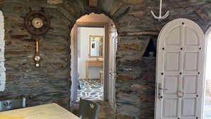 A stone-walled dining area with a wooden table and chairs, a clock, and a door leading to another room. - The Stone Windmill (Kea)