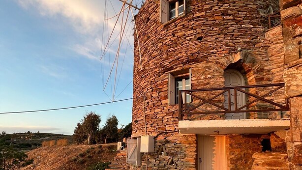 A stone house with a balcony, lounge chairs, and a table. - The Stone Windmill (Kea)