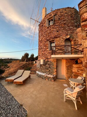A stone house with a balcony, lounge chairs, and a table. - The Stone Windmill (Kea)
