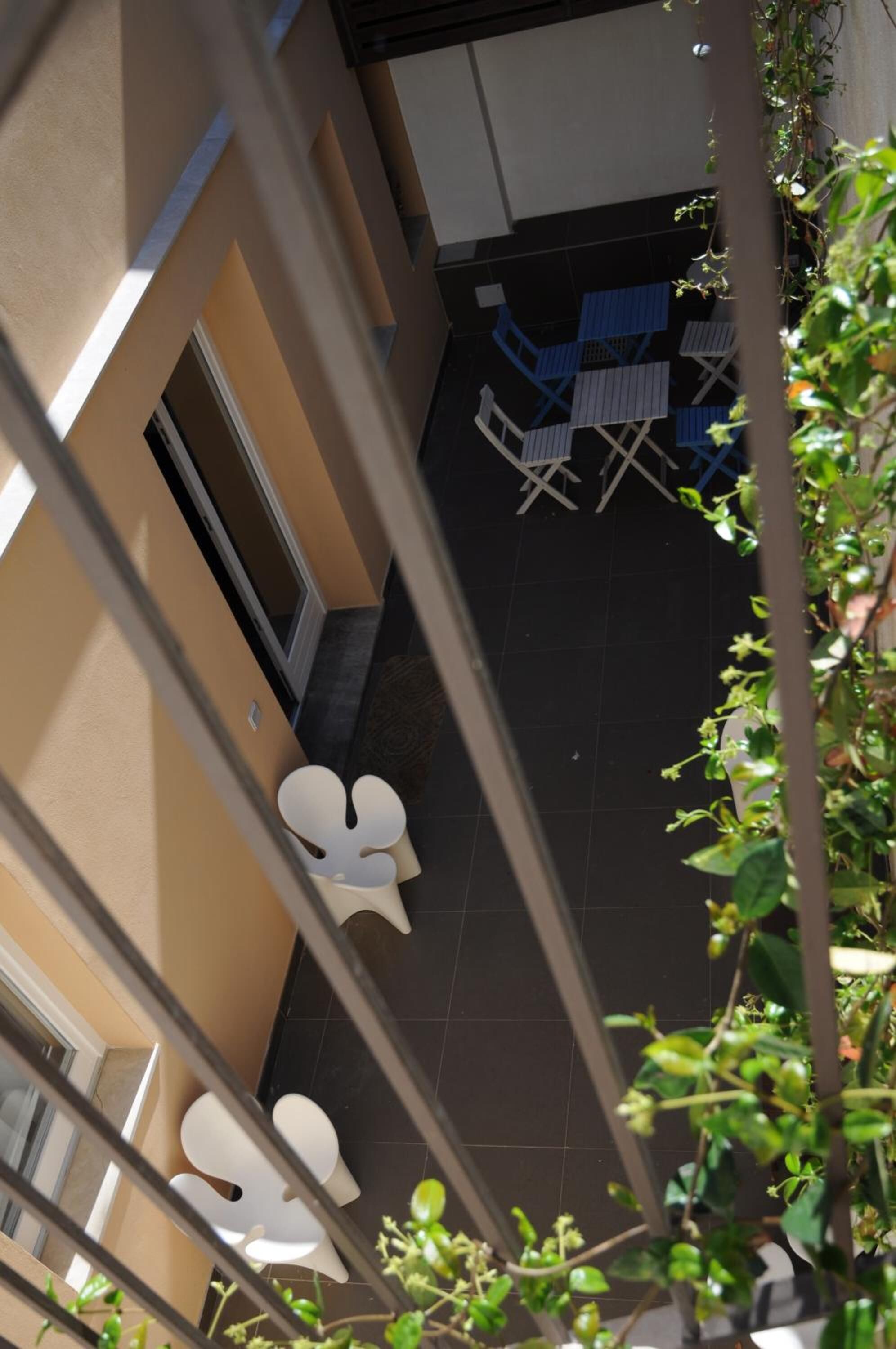 A balcony with white chairs and a table, surrounded by plants and a tiled floor.