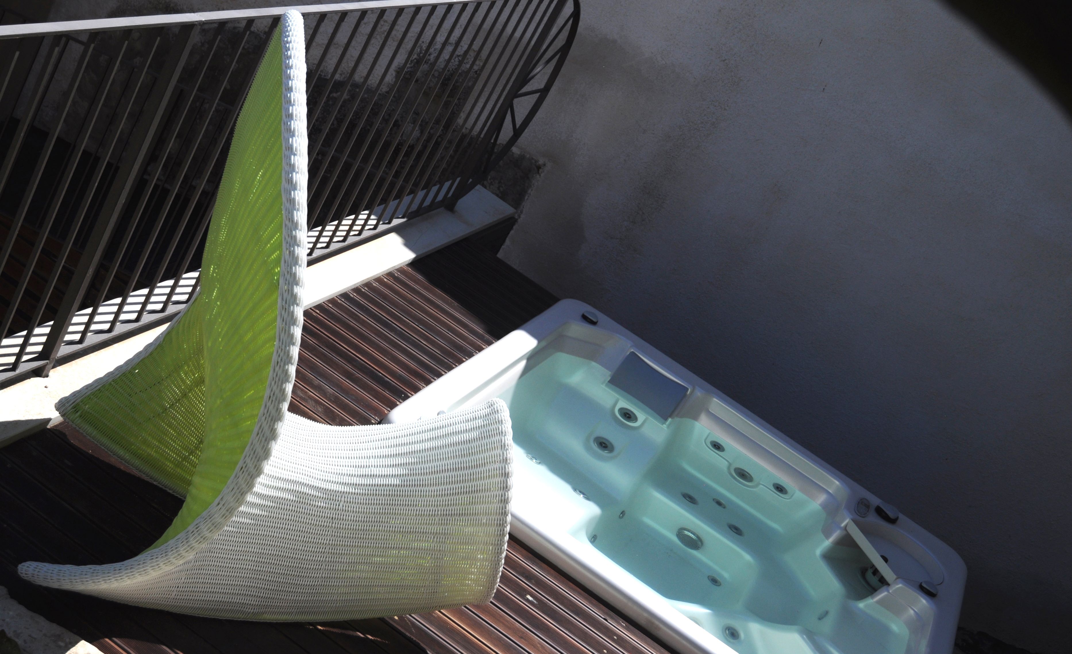 Un bain à remous sur une terrasse en bois, avec un mur blanc en arrière-plan.