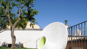 A modern outdoor swimming pool with a unique white, ribbed structure in the center, surrounded by a clear blue sky and a tree. - Iblainsuite (Ragusa)