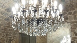 A stone-walled room with a wooden dining table, a chandelier, and a large mirror. - Iblainsuite (Ragusa)