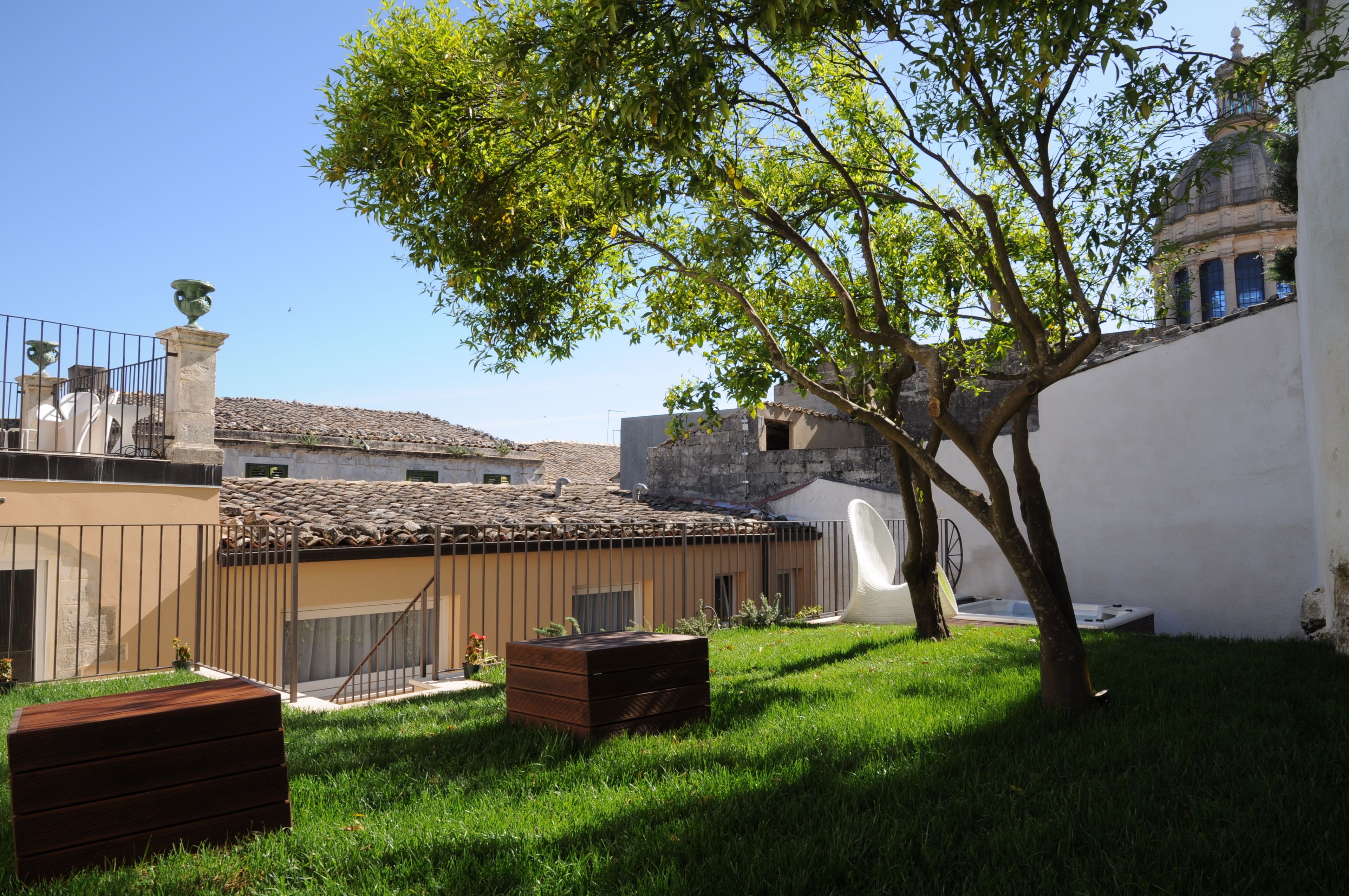 A courtyard with a tree, a white wall, and a building with a tiled roof.