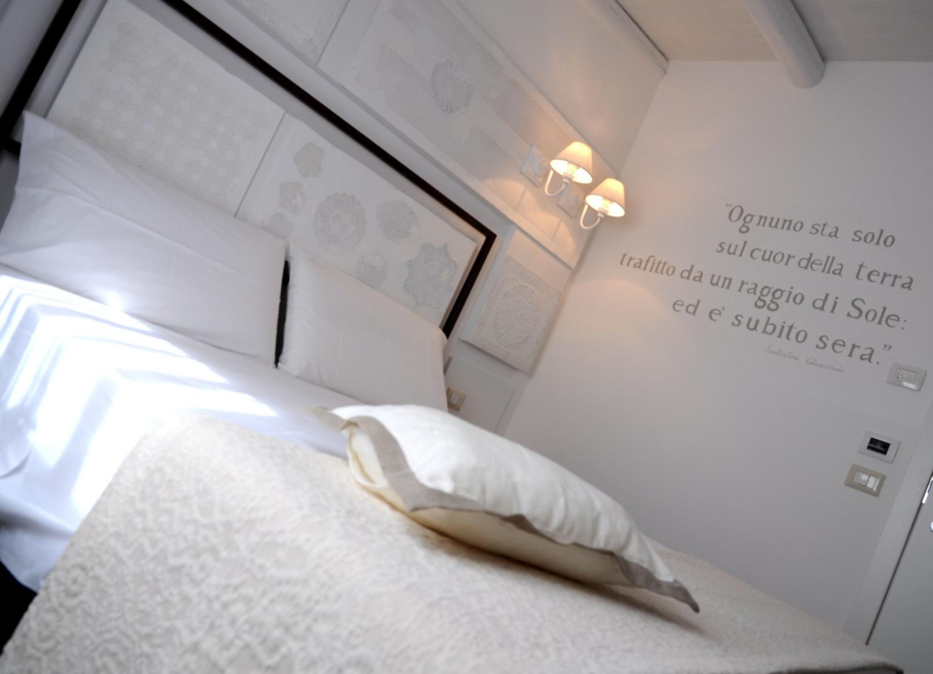 Una camera da letto con un letto, cuscini, una parete con una citazione e un lampadario.