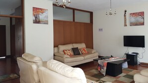 A living room with a sofa, a coffee table, a TV, and a chandelier. - Lolos Elegant Three Bedroom Apartment (Harare)