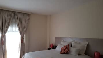 A neatly made bed with white and orange bedding, a red vase, and a patterned rug.