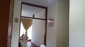 A hallway with a door leading to a living room. The room has a beige sofa, a white cushion, and a framed picture on the wall. - Lolos Elegant Three Bedroom Apartment (Harare)