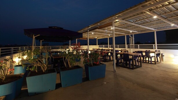 Un espace extérieur aménagé en terrasse, avec des tables et des chaises, des plantes en pot et un coin salon abrité.