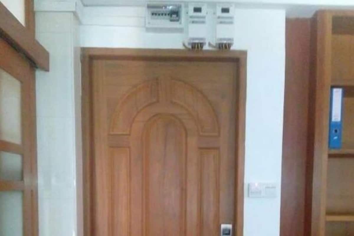 A wooden door with a handle and a lock, a white wall with a thermostat, and a wooden bookshelf.