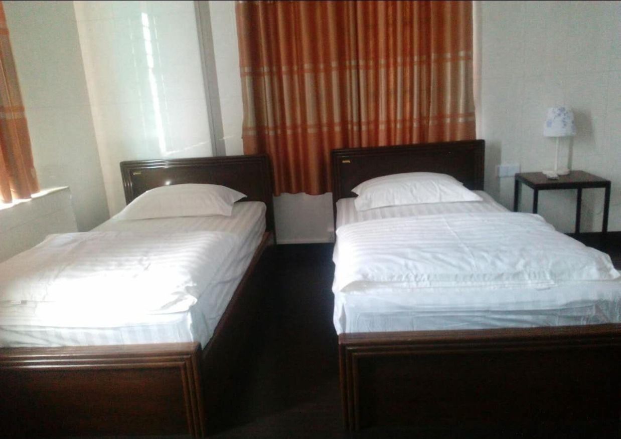 A hotel room with two single beds, a nightstand with a lamp, and a window with curtains.