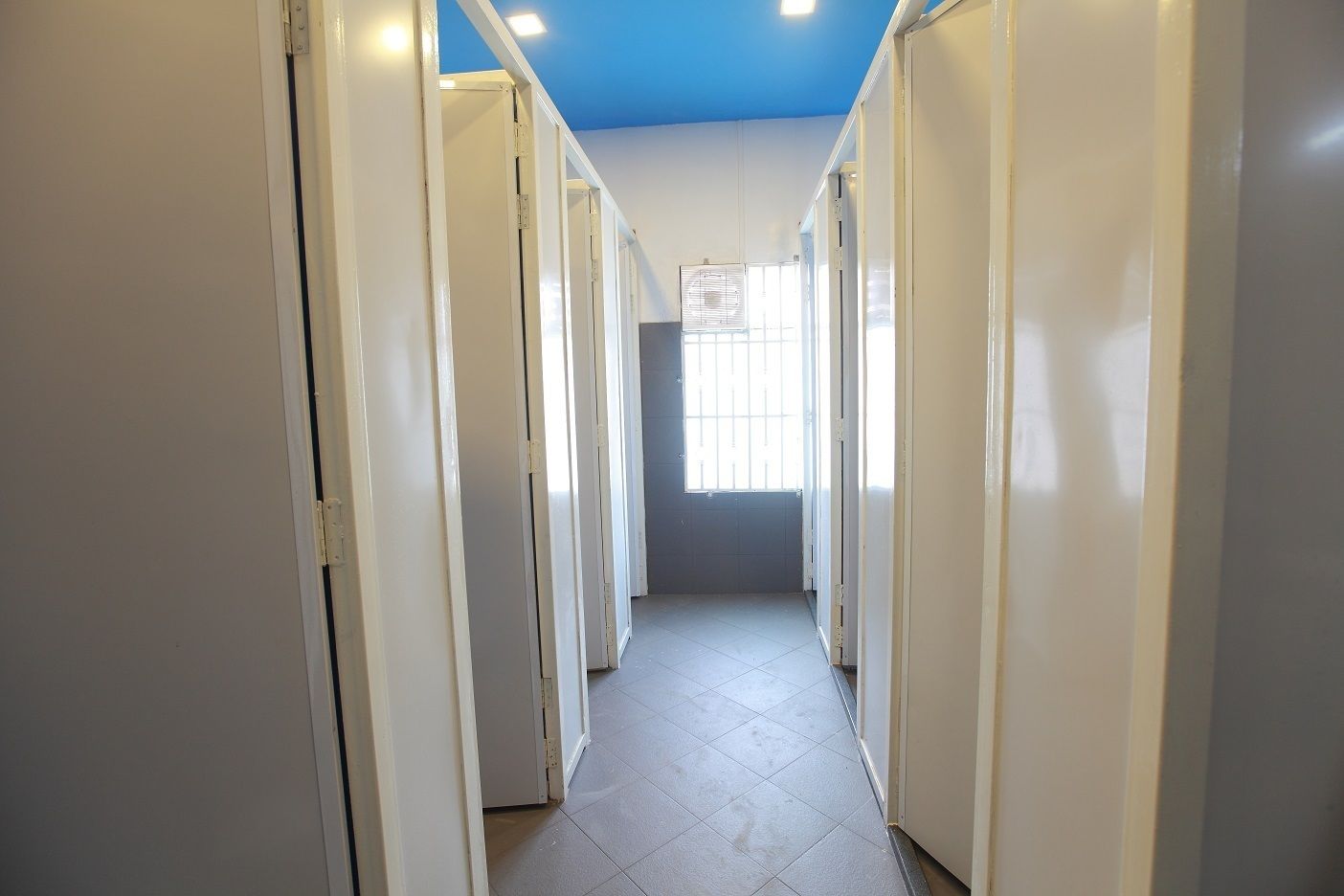 A corridor with white doors, a tiled floor, and a window at the end.