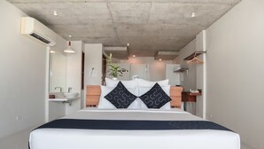 A modern hotel room with a large bed, a wooden headboard, a bedside table, a hanging plant, a bathroom with a sink and mirror, and a wardrobe.