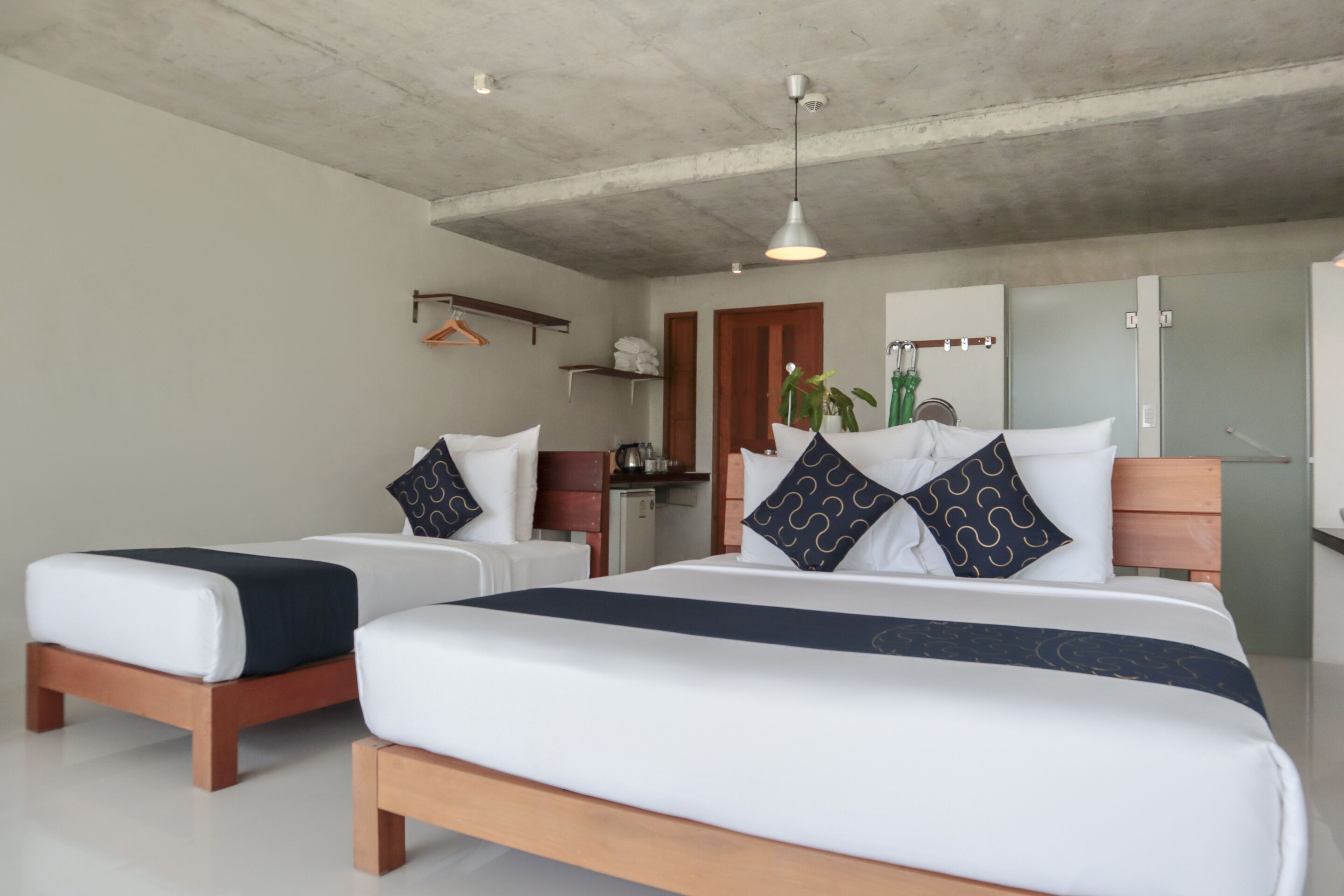 A hotel room with two beds, a wooden headboard, a hanging light fixture, and a small kitchenette.