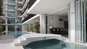 A modern hotel with a swimming pool, outdoor seating, and a balcony with plants.