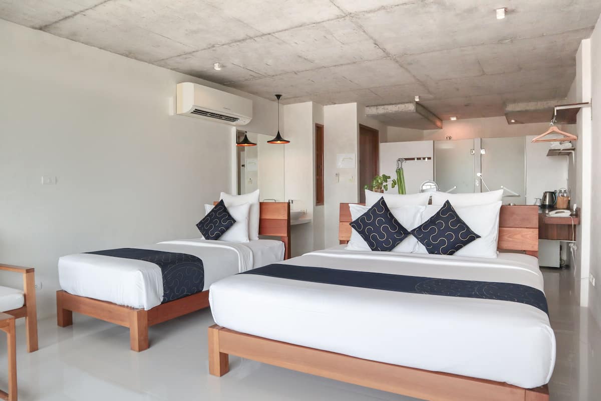 Une chambre d’hôtel avec deux lits, une tête de lit en bois, un petit bureau et un porte-vêtements.