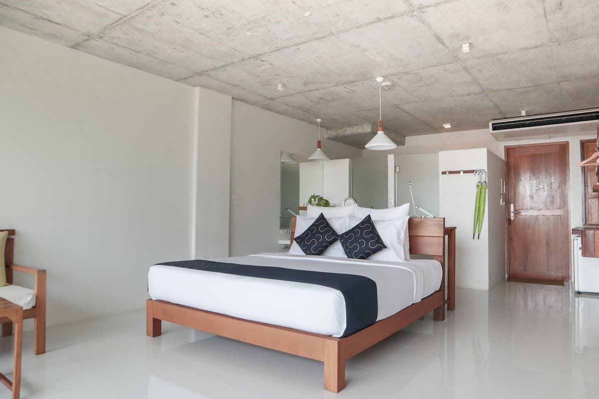 Une chambre moderne avec un lit en bois, des murs blancs et un plafond en béton.