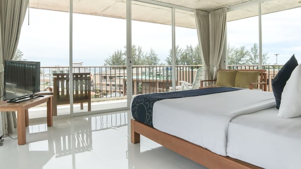 A modern hotel room with a large bed, a TV on a wooden table, and a balcony with a view of the city and trees.