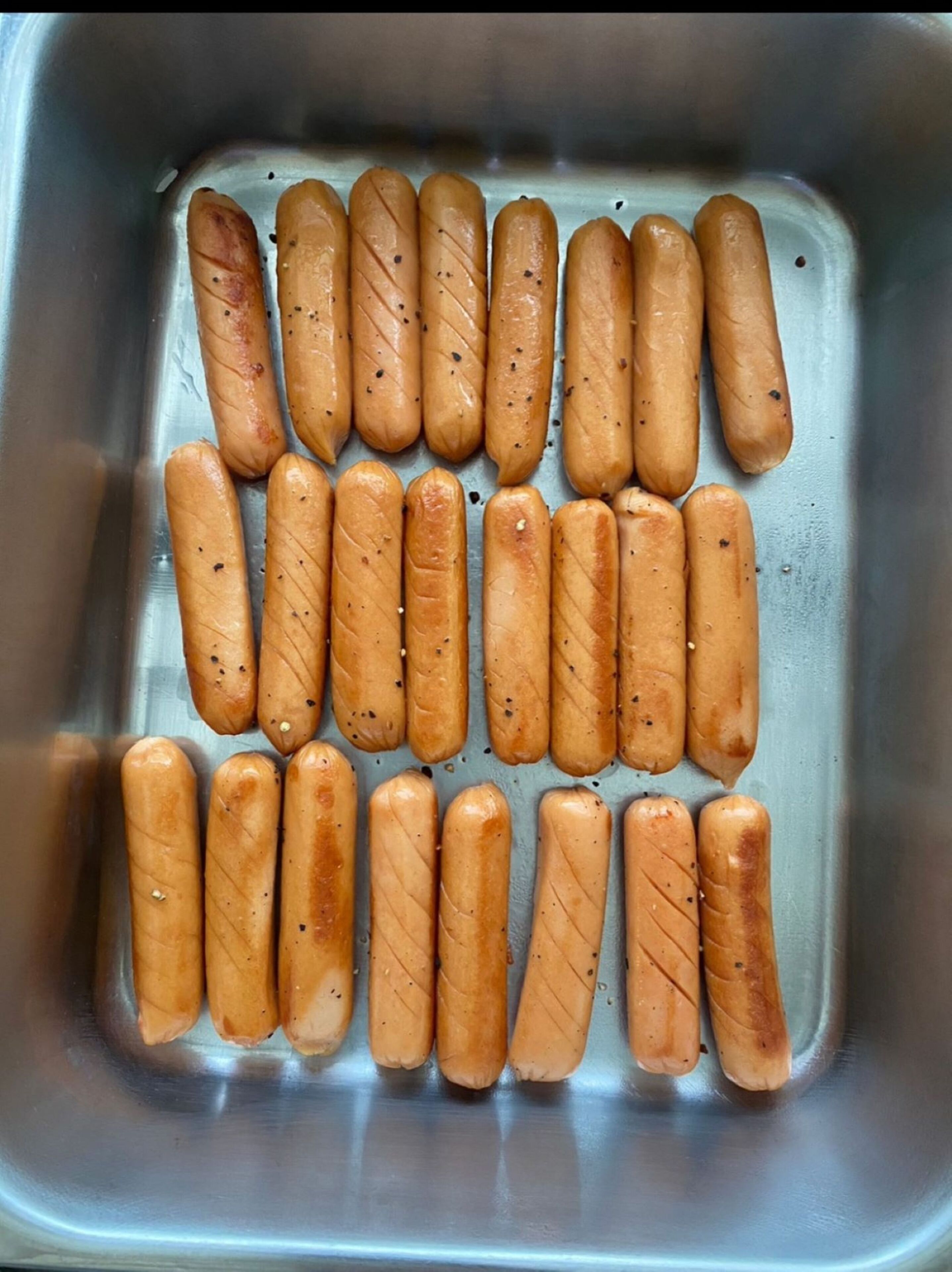 A stainless steel sink with multiple sausages arranged neatly in rows.