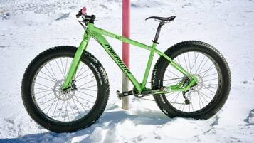 A green mountain bike with the brand name 'MERIDA FAT SIX' parked on snow.