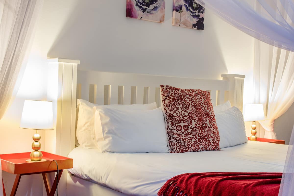 A neatly made bed with white and patterned pillows, a red throw blanket, and a bedside table with a lamp.