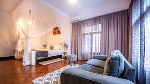 A room with a large sofa, a small table, a decorative rug, a bed with a canopy, and a window with curtains. - Sommerschield Guest House & Restaurant (Maputo)