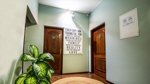 A hallway with wooden doors, a large potted plant, a woven rug, and a motivational quote on the wall. - Sommerschield Guest House & Restaurant (Maputo)