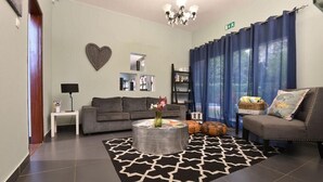 A living room with a grey sofa, a round coffee table with a vase, a patterned rug, and a bookshelf. - Sommerschield Guest House & Restaurant (Maputo)