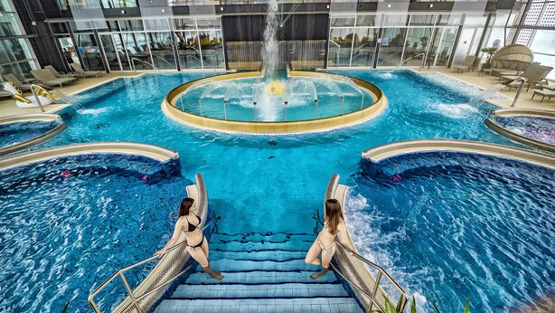 A large indoor swimming pool with multiple sections, including a central fountain area and surrounding water features. - Hotel Aquacity Riverside (Poprad)