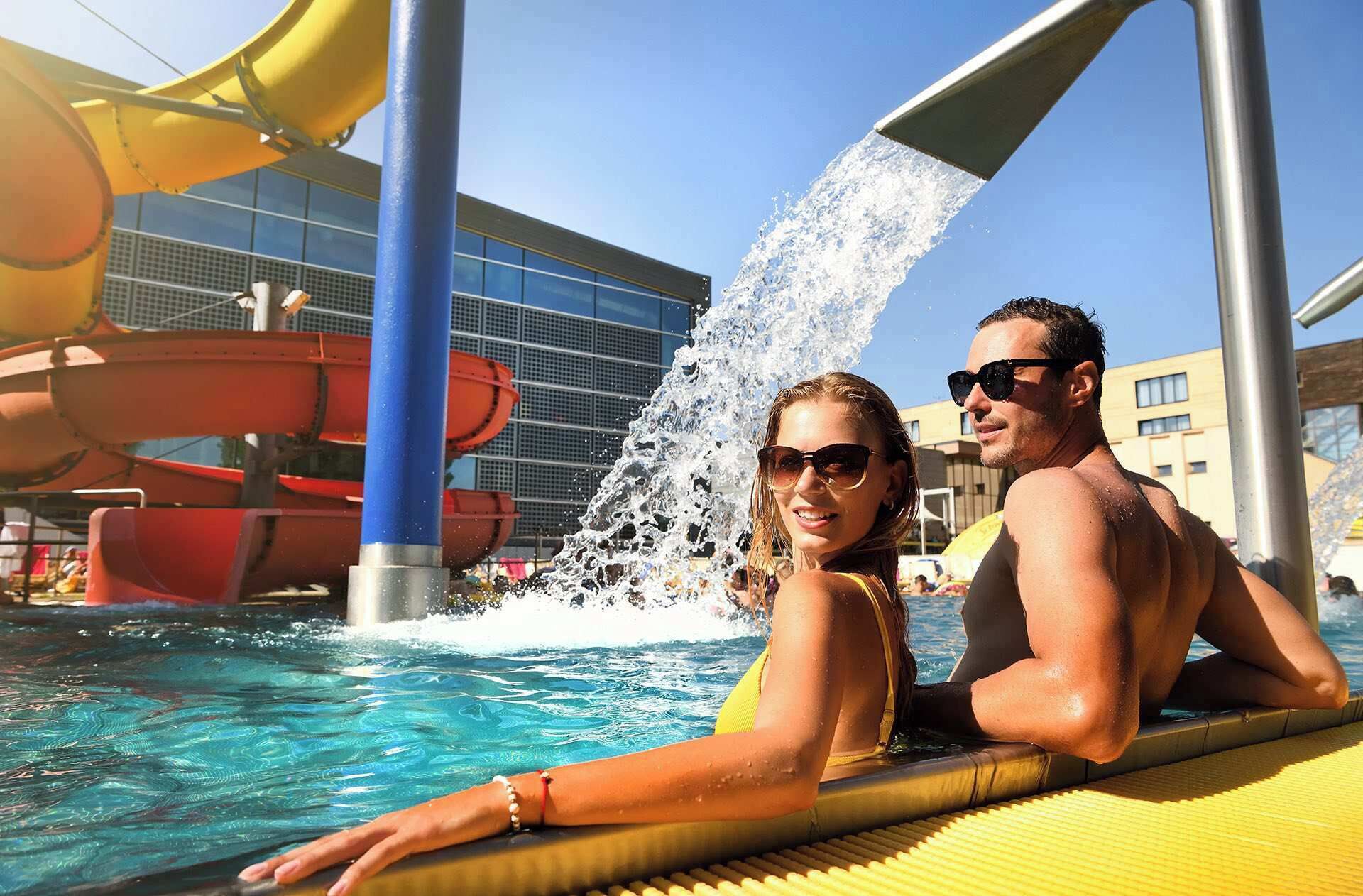 Zona de piscina con toboganes de agua y un edificio moderno al fondo.