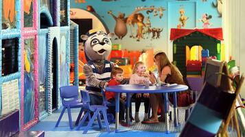 A play area with a mascot, children, and adults at a table.