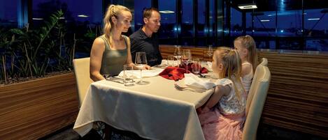 A family dining at a restaurant with a view of the cityscape at dusk.