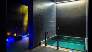 A modern bathroom with a glass-enclosed hot tub, dark tiled walls, and a blue-lit corner. - Hotel Aquacity Riverside (Poprad)