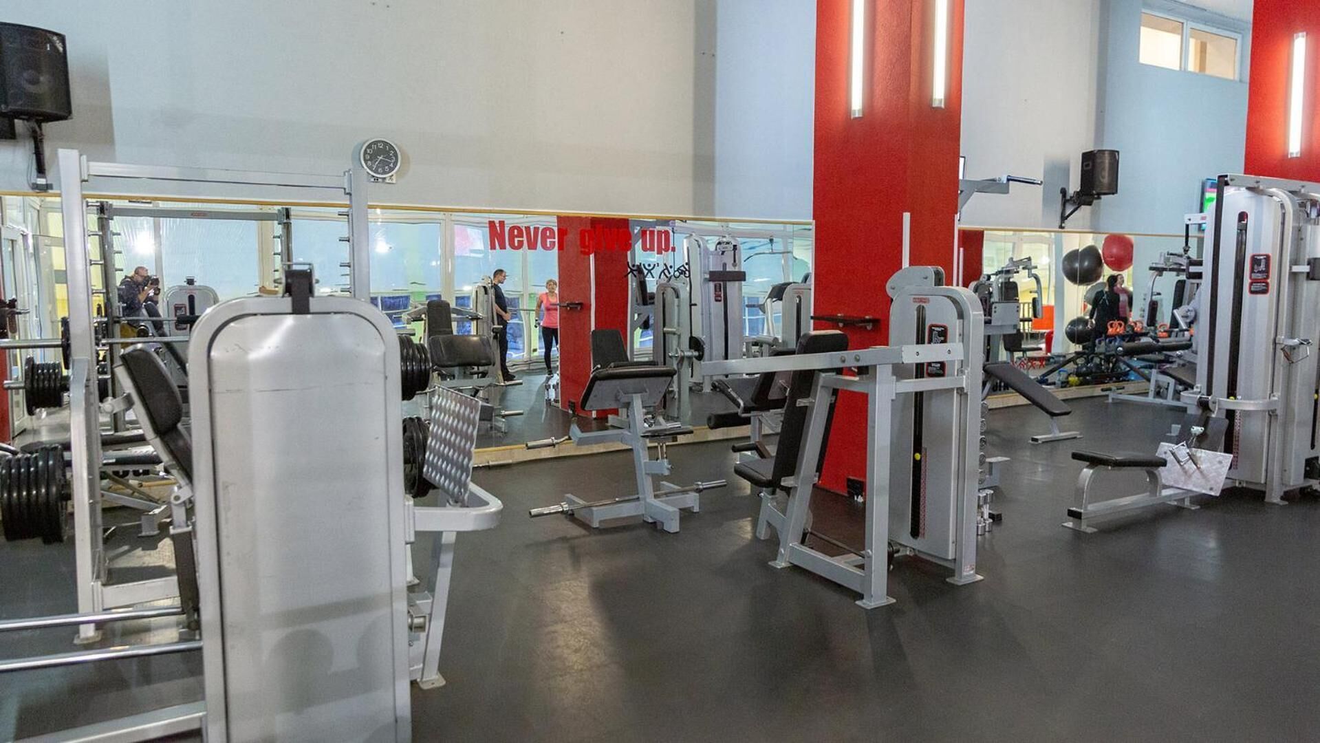 A gym with various exercise equipment, a clock on the wall, and a motivational sign.