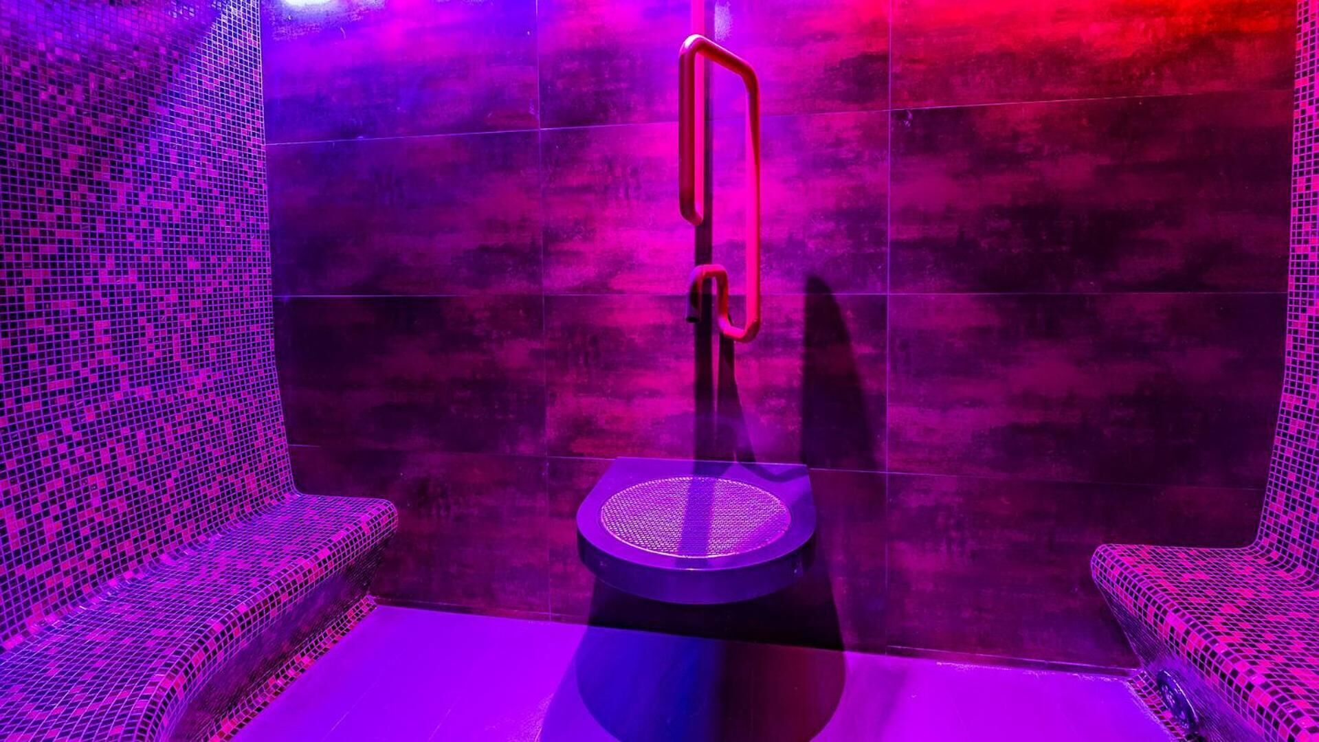 A modern sauna with a central bench and a handrail, surrounded by tiled walls.