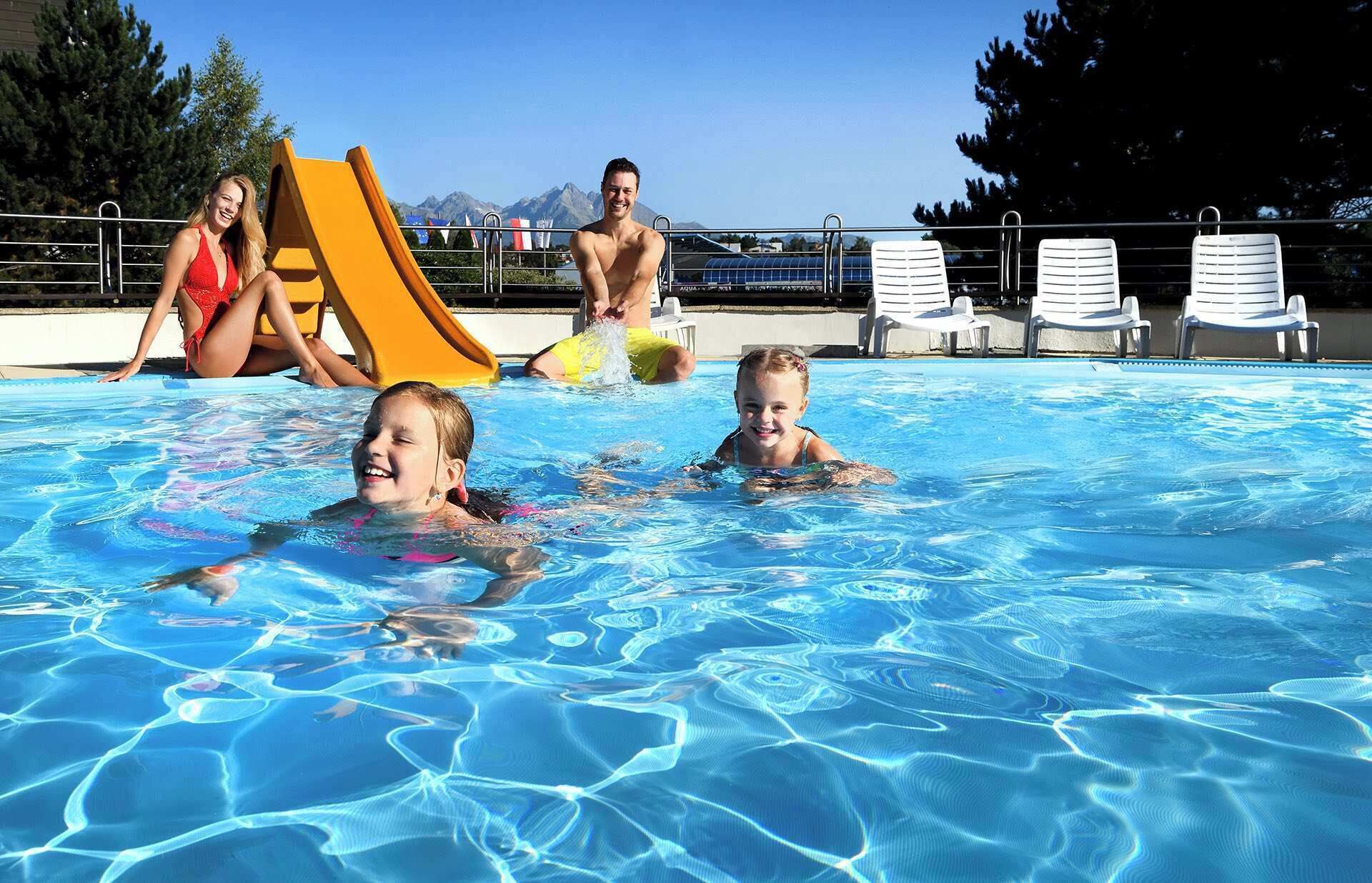 A swimming pool with clear blue water, a yellow slide, and white lounge chairs.