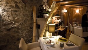 Un comedor con paredes de piedra, una mesa dispuesta con platos, cubiertos y una vela.