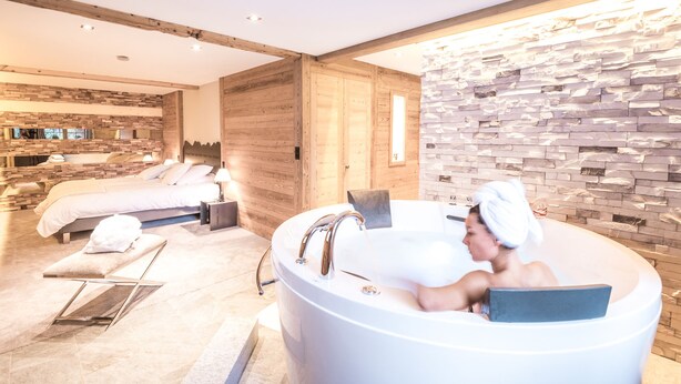 Un baño moderno con una bañera independiente, una pared de madera y una cama en la habitación contigua.