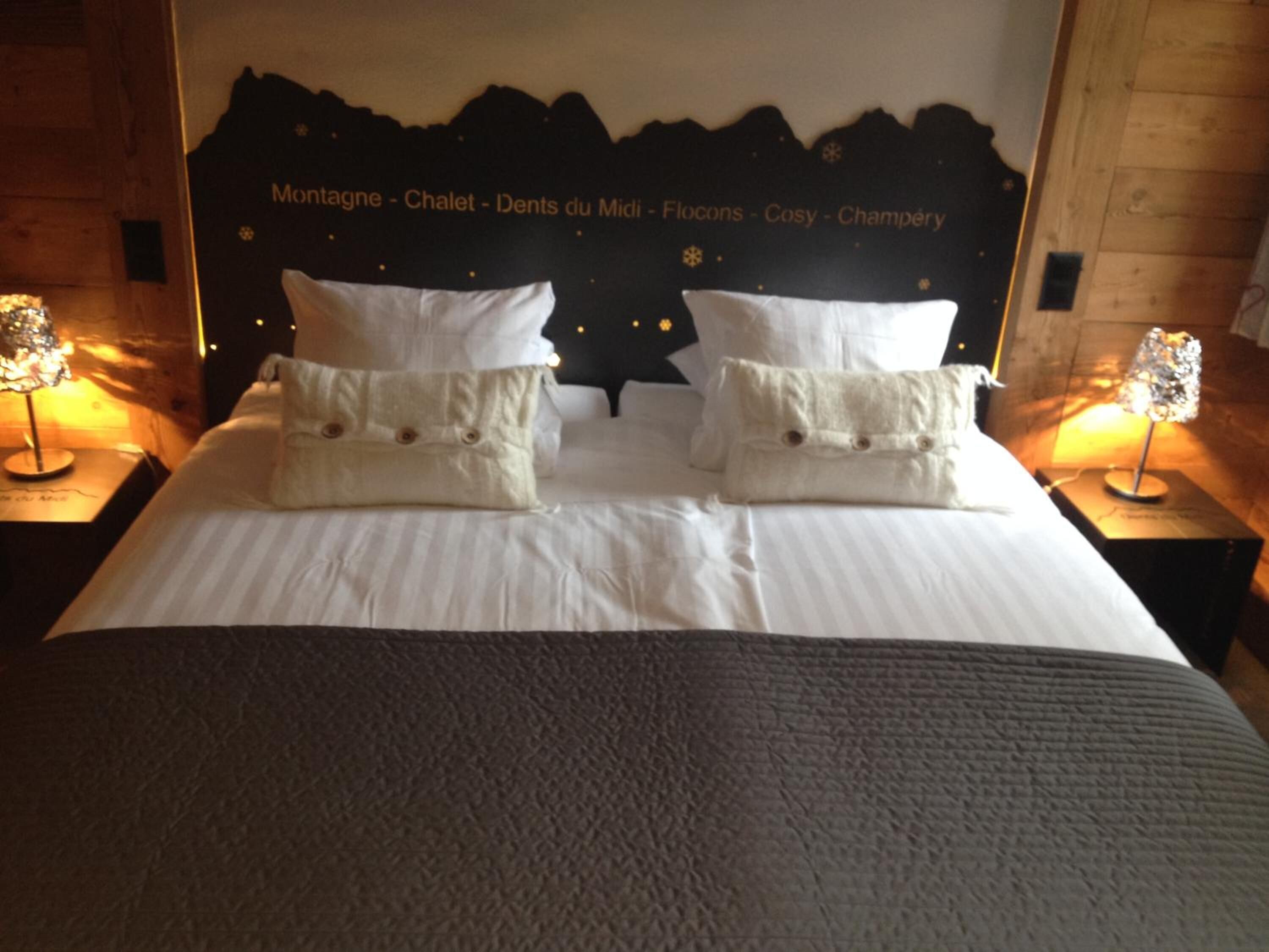 A neatly made bed with white linens and two pillows, a dark headboard with text, and two bedside lamps on wooden nightstands.