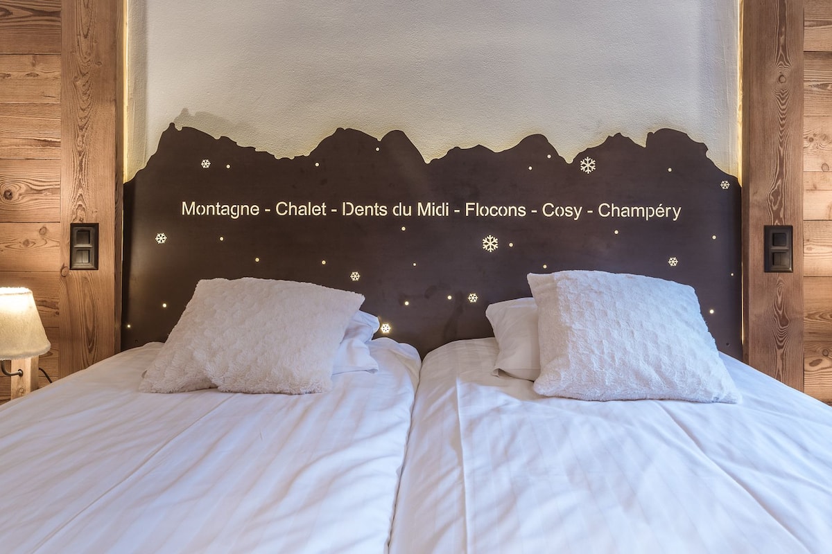 A bed with white linens and two pillows, a wooden headboard with a mountain silhouette, and two bedside lamps.