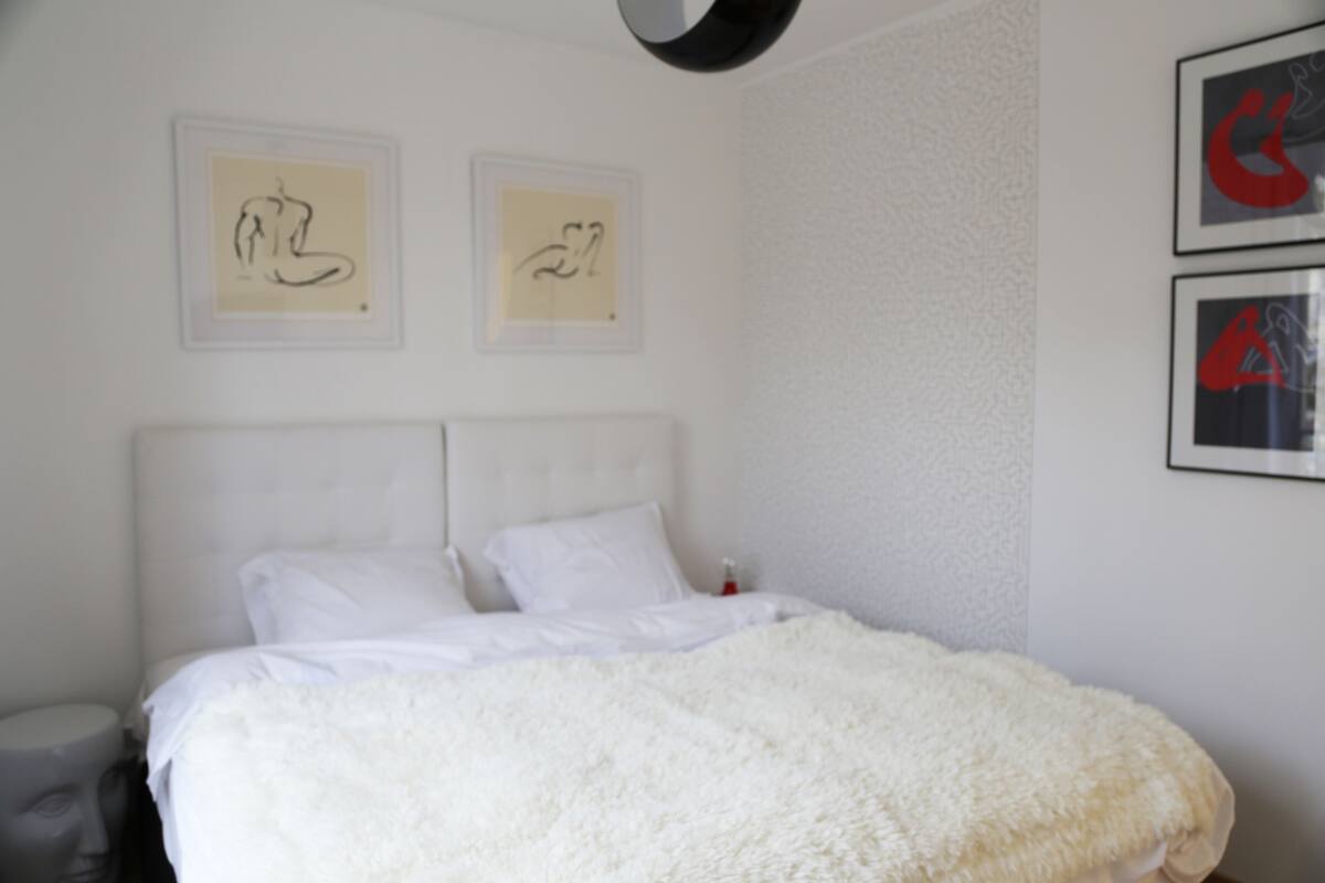 Ein Schlafzimmer mit einem weißen Bett, einer weißen Kopfteil und zwei gerahmten Kunstwerken an der Wand.
