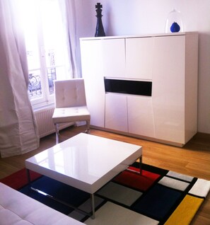 Una sala de estar moderna con un sofá blanco, una mesita de centro blanca, un mueble blanco y una alfombra colorida.
