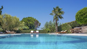 A clear blue pool with lounge chairs and a palm tree. - Sitia Oceanides (Sitia)