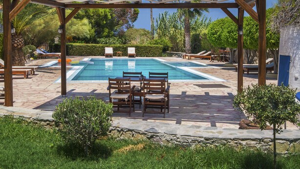 A pool area with a pergola, lounge chairs, and a stone patio. - Sitia Oceanides (Sitia)